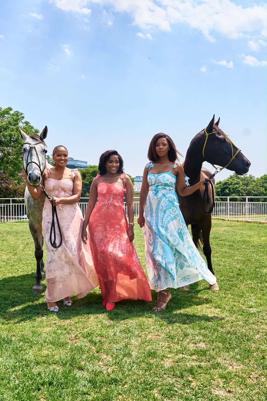Three women in pastel pink, coral and aqua dresses with two horses