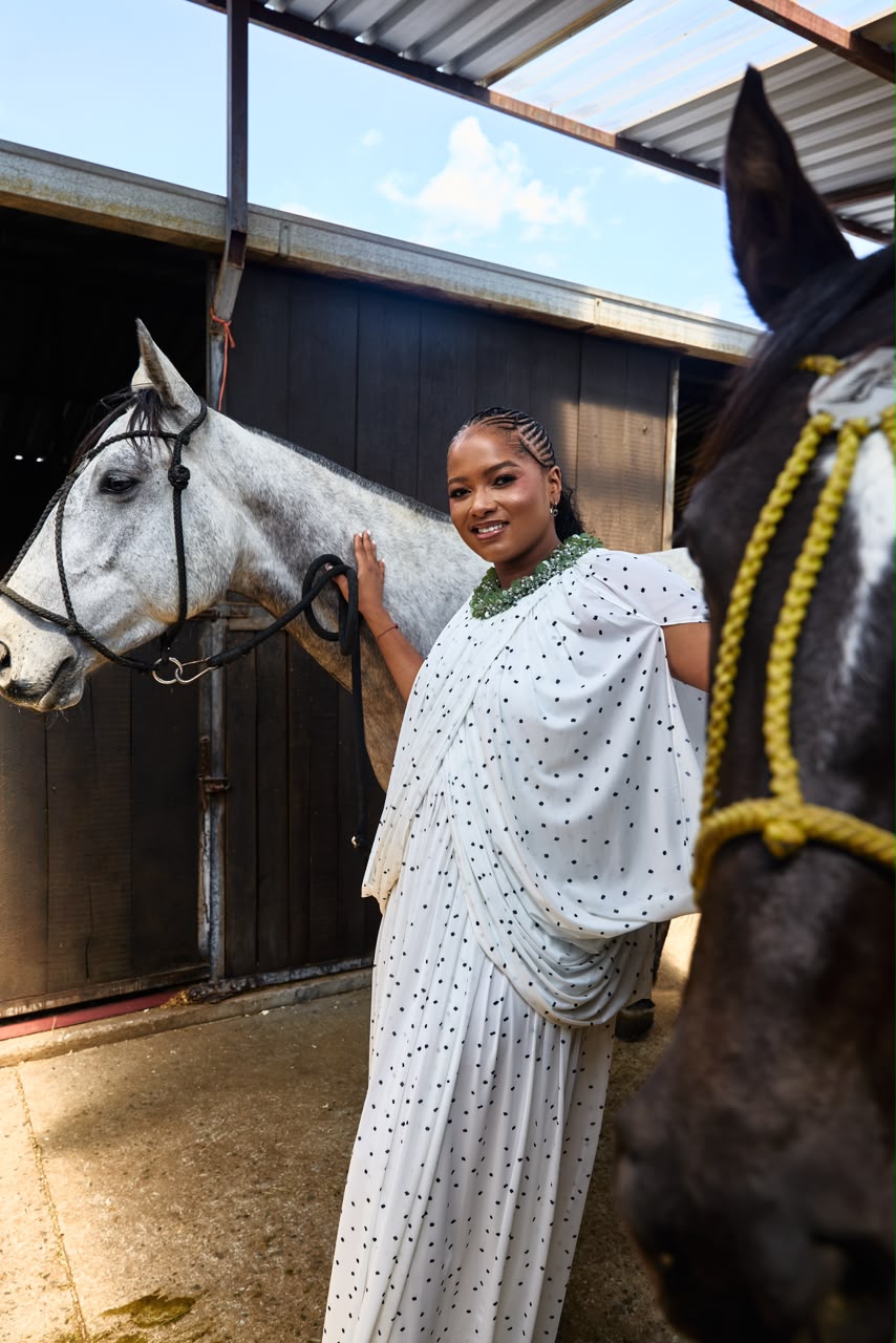 Woman in a white polka-dot draped dress at the stables
